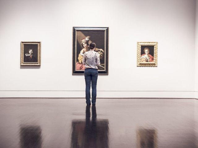 kobieta w muzeum przed trzema obrazami zawieszonymi na ścianie
