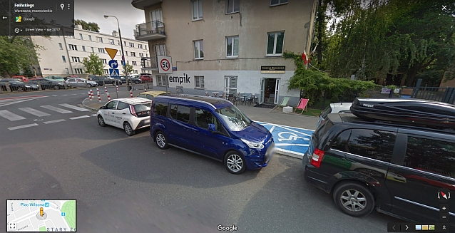 Widok na dwie niebieskie koperty, które są zastawione z każdej strony przez parkujące na ulicy samochody