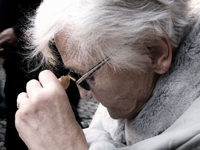 starsza pani z profilu z podniesioną ręką którą trzyma kawałek chleba