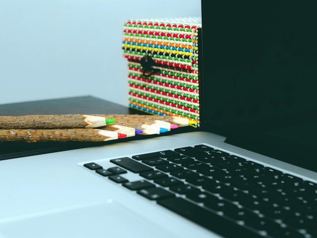 laptop stoi na stole, obok leżą kolorowe kredki i stoi kolorowe pudełko