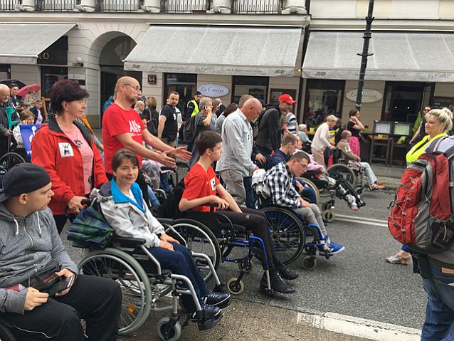 Uczestnicy protestu idą ulicą. Rząd osób na wózkach, za nimi opiekunowie
