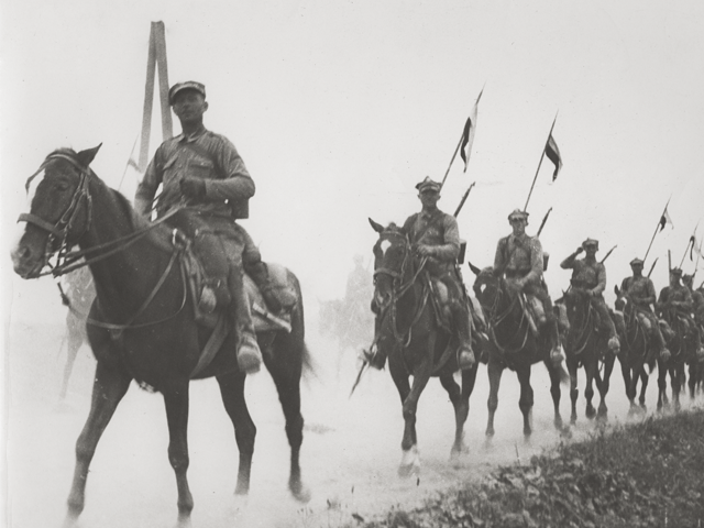 Oddział kawalerii jedzie konno wzdłuż drogi. 