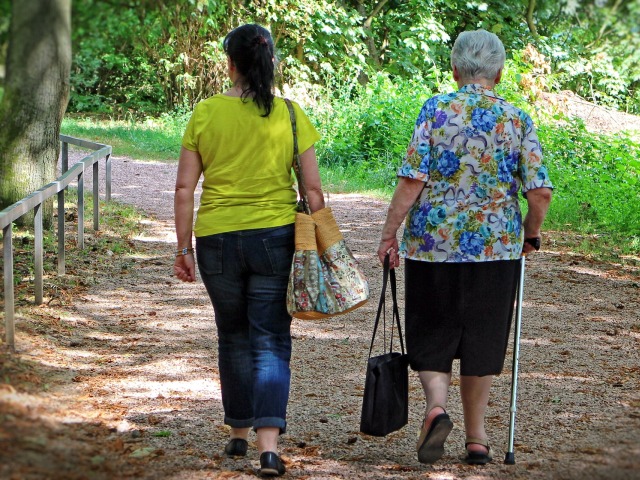 starsza kobieta z kulą i torebką w drugiej ręce obok młodsza kobieta z torebką na ramieniu widziane od tyłu idą przed siebie