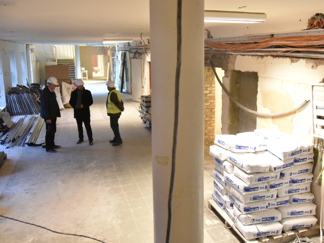 remont wewnątrz budynku widać worki z cementem i inne materiały budowlane posrodku stoi trzech mężczyzn w kaskach