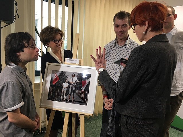 Minister Rafalska przy zdjęciu stojącym na sztaludze rozmawia z jego autorem i panią prezes PFRON