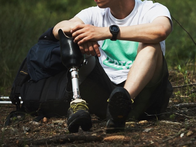 mężczyzna siedzi na ziemi w lesie, zbliżenie na nogę i protezę nogi