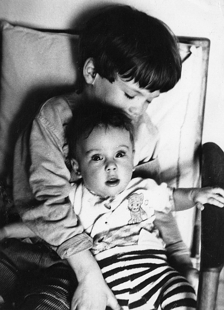 Chłopiec trzyma na kolanach dziewczynkę, która ma około roczku