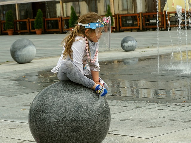 dziewczynka w przyłbicy obok fontanny siedzi na kamiennej kuli