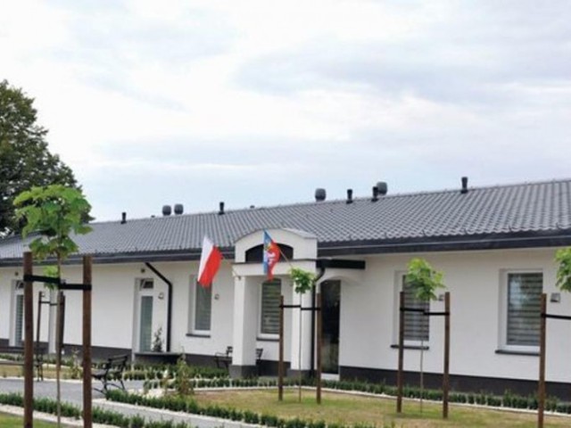 biały parterowy budynek z flagami przed wejściem, com w jaszczowie