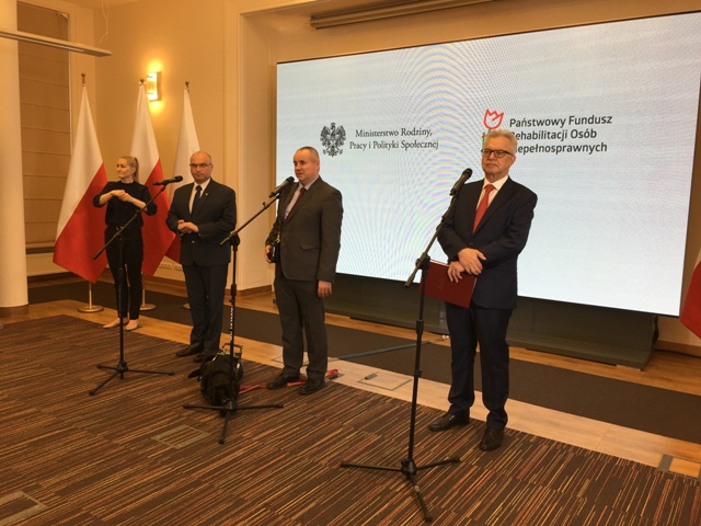 przy mikrofonach podczas konferencji stoją od prawej tłumaczka języka migowego, Stanik, Wdówik i Michałkiewicz
