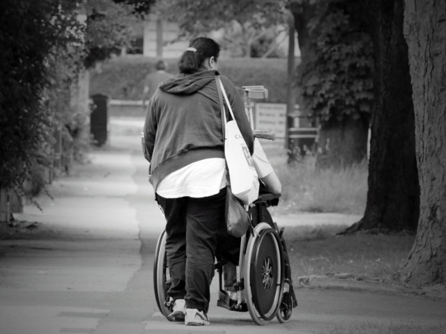 kobieta pcha wózek z osobą niepełnosprawną