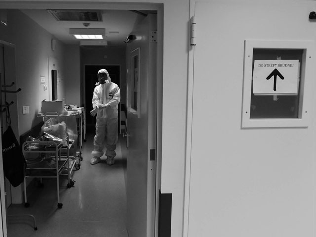 medyk w białym skafandrze na korytarzu. na drzwiach napis wejście do strefy brudnej