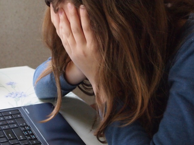 dziewczynka nastolenia z głową ukytą we włosach oparta na rękach siedzi przy laptopie przy stole