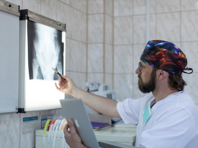 Andrzej Kupilas w lekarskim kitlu i czepku przy zdjęciu rentgenowskim wskazuje coś długopisem