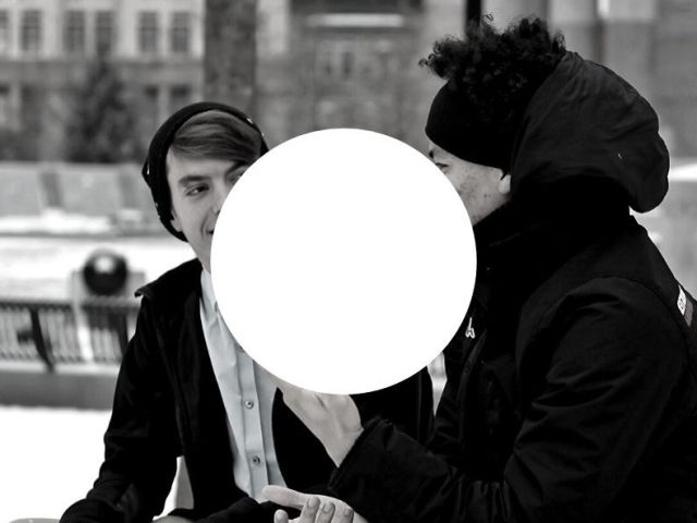 czarno białe zdjęcie dwóch uśmiechniętych mężczyzn zwróconych ku sobie na części ich twarzy pośrodku zdjęcia biały okrąg