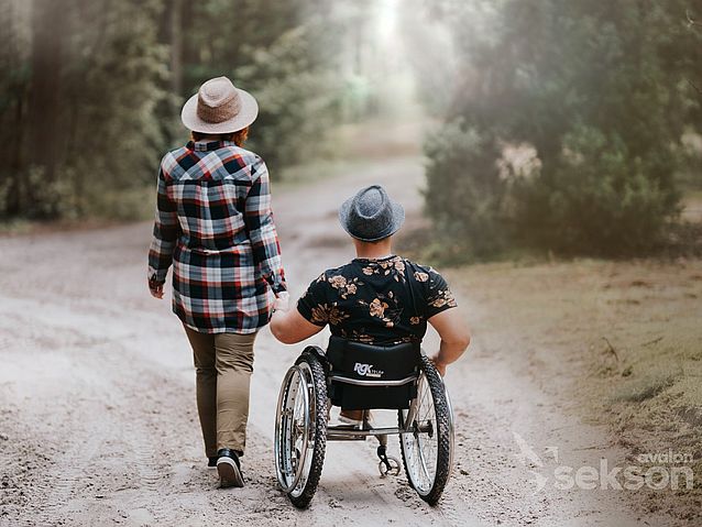 Trzymający się za ręce pełnosprawna kobieta i mężczyzna na wózku idą leśną piaszczystą drogą