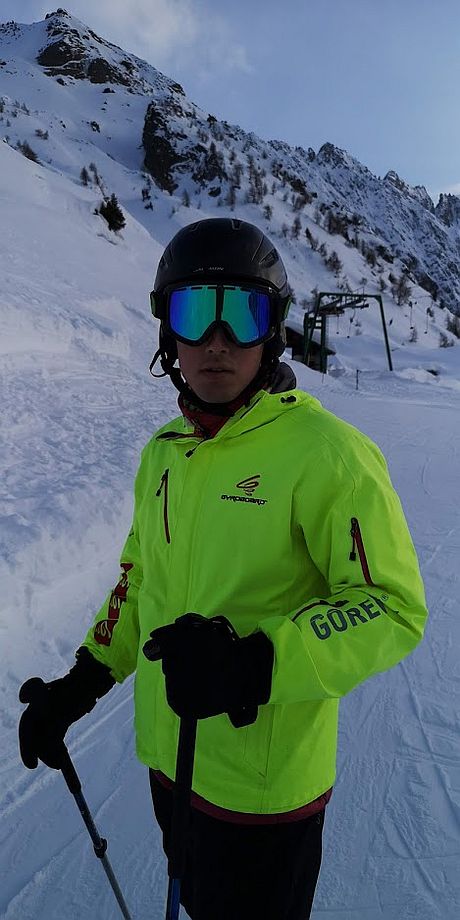 Wojciech w kurtce narciarskiej, kasku i goglach pozuje do zdjęcia na tle gór