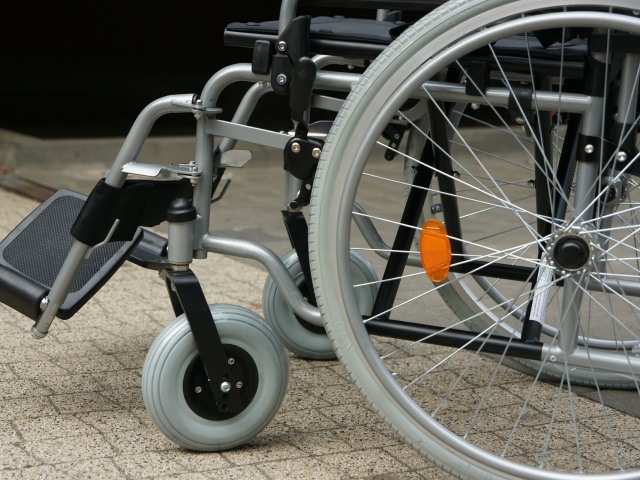wózek inwalidzki stoi na chodniku widać przód i koło