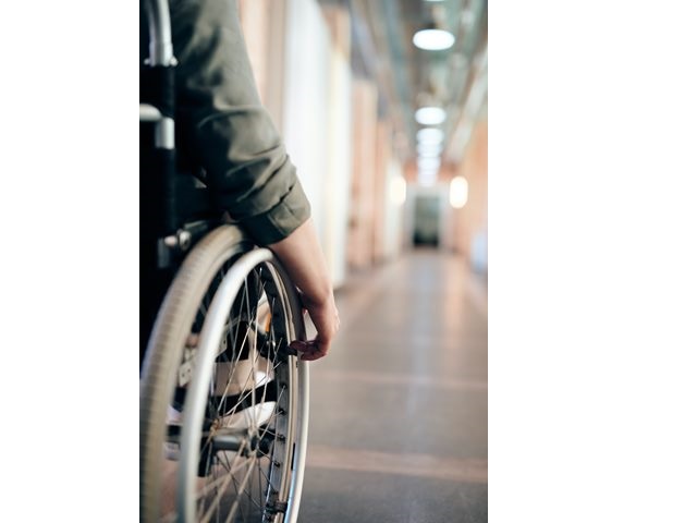 kobieca ręka na kole wózka inwalidzkiego na korytarzu