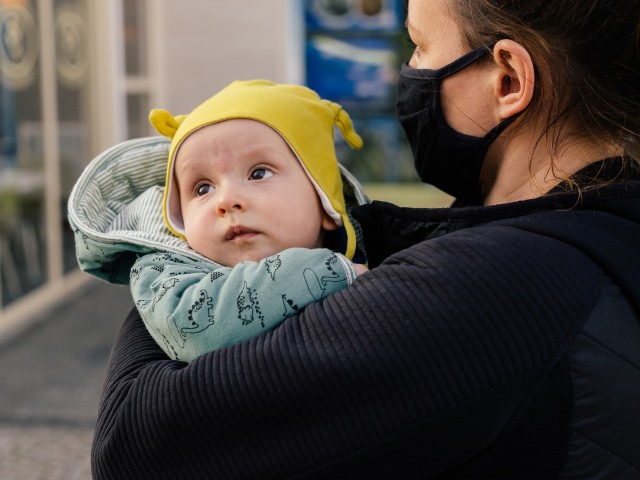 kobieta w maseczce na ulicy trzyma w ramionach małe kilkumiesięczne dziecko