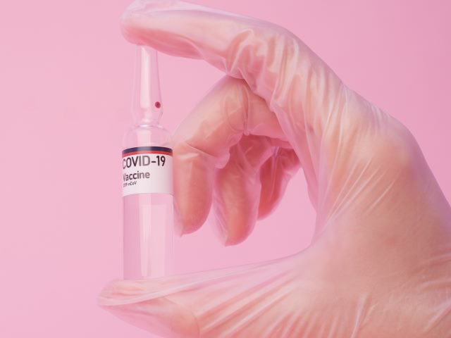 ręka w gumowej rękawiczce trzyma buteleczkę z napisem covid-19 vaccine