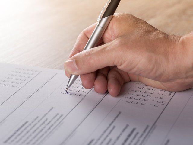 ręka trzyma długopis i wypełnia ankietę zaznaczając po prawej jej okienka