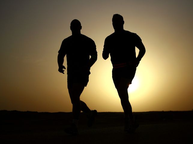 Sylwetki dwóch mężczyzn biegnących w zachodzącym słońcu