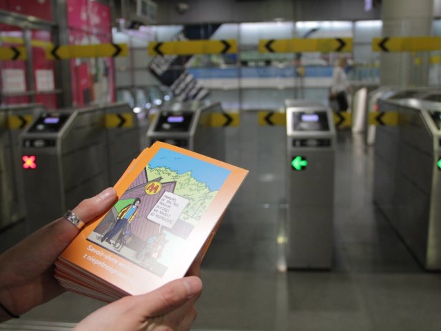 kobiece ręce trzymają broszurę Integracji savoi-vivre wobez osób z niepełnosprawnością w tle bramki do metra