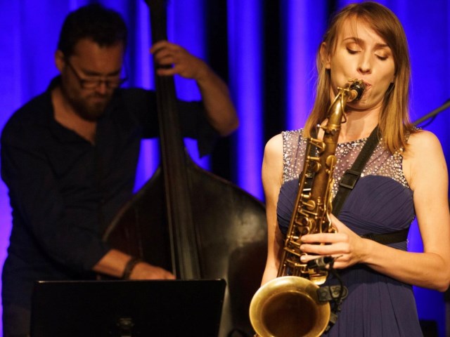 Karolina Pernal gra na saksofonie w czasie występu na scenie w tle inny muzyk towarzyszący