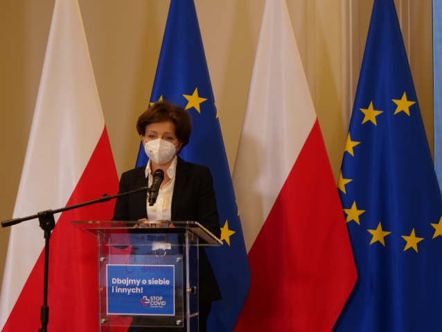 minister Marlena Maląg w maseczce przemawia z mównicy na tle flagi Polski i UE