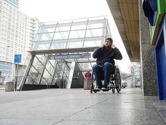 mężczyzna na wózku jedzie chodnikiem w Warszawie w tle stacja metra Warszawa Gdańska