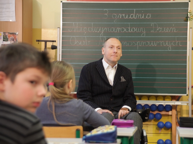 Piotr Pawłowski prowadzi w szkole zajęcia dla dzieci w tle tablica z napisem 3 grudnia międzynarodowy dzień osób niepełnosprawnych