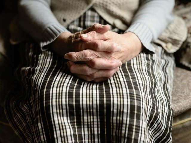 starsza kobieta trzyma złączone dłonie na spódnicy