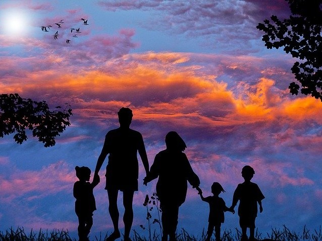 Rodzice z trójką dzieci trzymając się za ręce idą w stronę zachodzącego słońca