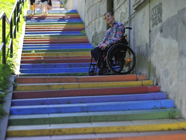 Wiktor Okrój na wózku na długich schodach z kolorowymi stopniami