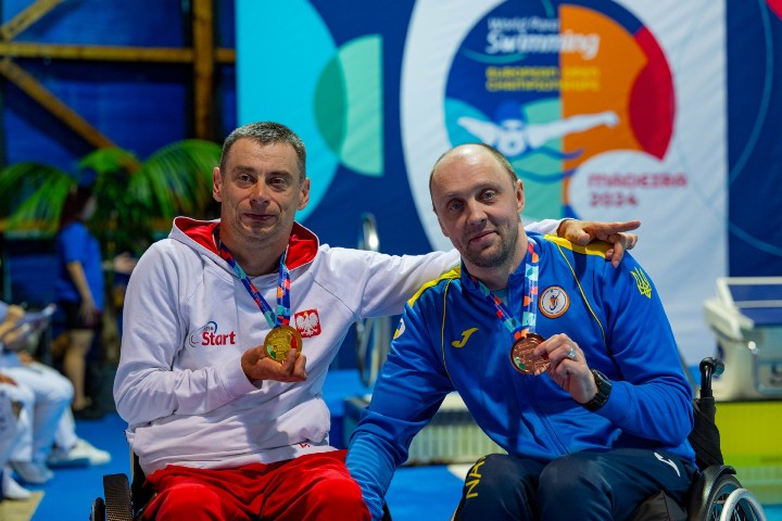 dwójka mężczyzn na wózkach, trzymają w dłoniach medale. 