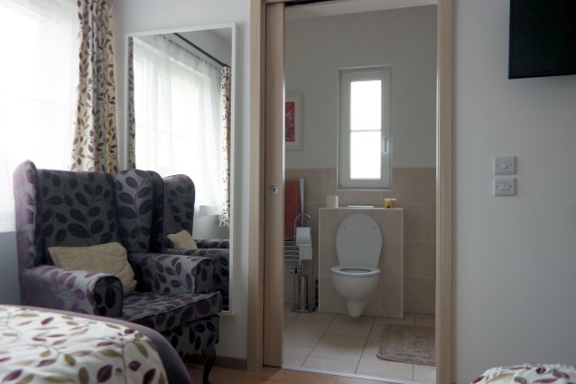 fragment pokoju - po lewej stronie stoi fotel, obok niego są otwarte drzwi do łazienki