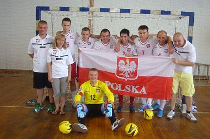 Zawodnicy i sztab szkoleniowy Polskiej Reprezentacji Diabetyków pozują do wspólnego zdjęcia w biało-czerwonych strojach piłkarskich, trzymając dużą flagę Polski. W tle bramka
