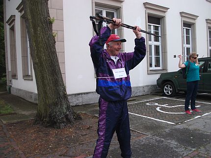 Starsi kobieta i mężczyzna stoją na parkingu trzymając w górze nad głową kijki do nordic walkingu