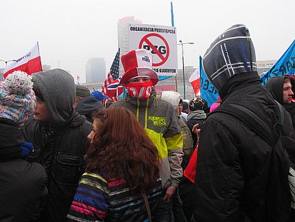 Manifestacja. Mężczyzna z biało-czerwonym szalikiem na twarzy. W tle transparent z przekreśloną nazwą PZG.