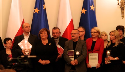 Anna Komorowska wraz z laureatami konkursu na tle flag Polski i Unii Europejskiej