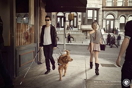 Plakat kampanii: niewidomy mężczyzna idzie ulicą, jego pies przewodnik ogląda się za krótką spódniczką młodej dziewczyny