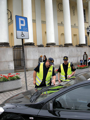 Strażnicy miejscy sprawdzają kartę parkingową zaparkowanego na kopercie samochodu
