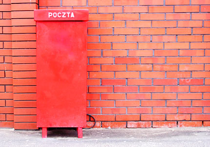 Czerwona skrzynka pocztowa stojąca na tle muru z cegieł