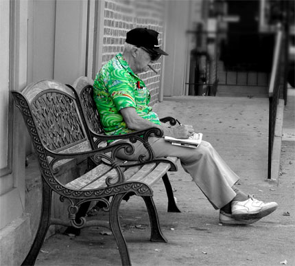 Starszy meżczyzna siedzący na ławce i rozwiązujący krzyżówkę