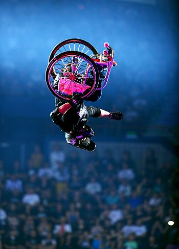 Aaron Fotheringham robi salto na wózku inwalidzkim, wózek jest u góry, głowa u dołu zdjęcia.