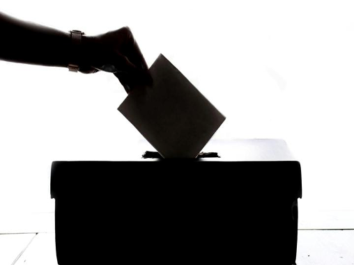 zdjęcie poglądowe. Czarno białe zdjęcie. Pudełko na głosy wyborcze. Widoczna jest dłoń, która wrzuca do pudełka kartkę z głosem. 